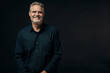 © Claes - Confident man with gray hair smiling in dark shirt against dark background portrait closeup