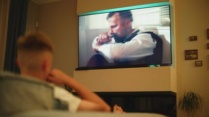 Poster - teenage boy lies on sofa in cozy living room and watching action movie on tv in the evening at home.