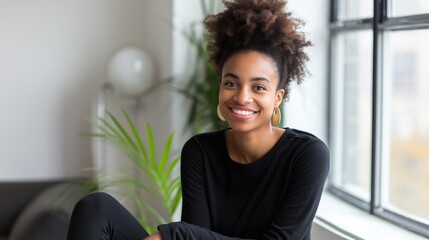 Wall Mural - Young Black woman with curly hair smiles and sits by window