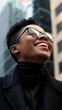 © ANC Media - Smiling Black woman in glasses looks up in a city setting