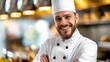 © Ananncee Media - A bearded chef in a white uniform stands in a restaurant kitchen with a smile