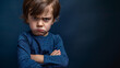 © Ikhou - A little boy stands with his arms crossed and looks at the camera, looking angry against a dark blue background