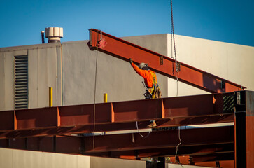 A consruction worker directing placement of a large steel beam that is atttached to a crane