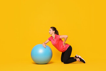 Wall Mural - Beautiful pregnant woman doing exercises with fitball on yellow background