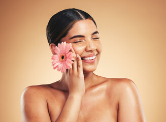 Skincare, smile and woman with flower in studio for beauty, wellness and organic cosmetics on brown background. Floral, dermatology and hand on face of model happy with plant, cosmetology or results