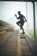 © DavisShared/peopleimages.com - Man, running and profile on stairs for fitness, health and cardio training to lose weight at stadium. African person, athlete and speed on steps, moving or balance for development with workout in fog