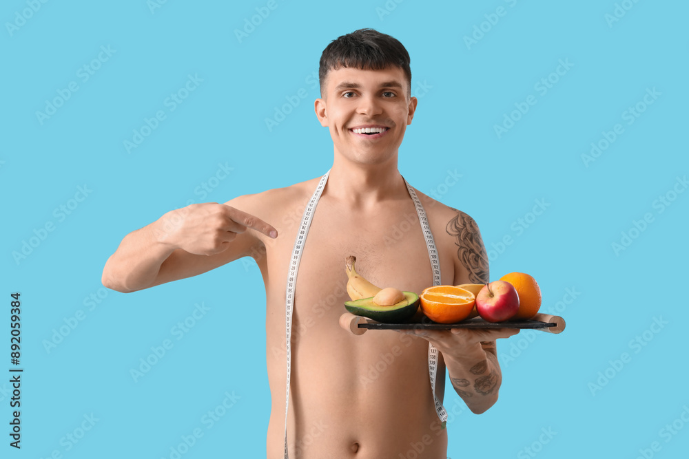 Young man with measuring tape and fruits on blue background. Diet concept