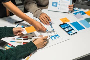 A group of people collaborates around a desk, discussing and reviewing user interface (UI) and user experience (UX) elements. usability, accessibility, and design principles for product development.