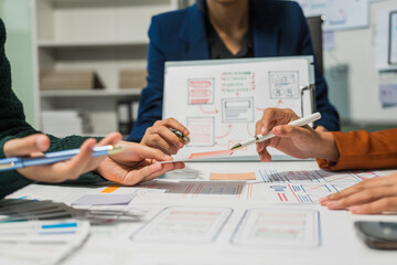 A group of people collaborates around a desk, discussing and reviewing user interface (UI) and user experience (UX) elements. usability, accessibility, and design principles for product development.