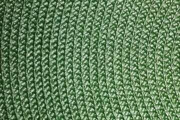 a close-up view of a green woven or knitted fabric. The texture is made up of tightly interlaced threads, creating a pattern of diagonal lines. The material appears to be thick and sturdy, possibly us