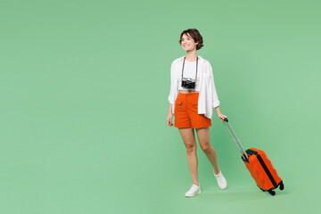 Wall Mural - Full body smiling happy traveler woman wears casual clothes hold suitcase bag walk go look aside isolated on plain green background. Tourist travel abroad in free time rest. Air flight trip concept.