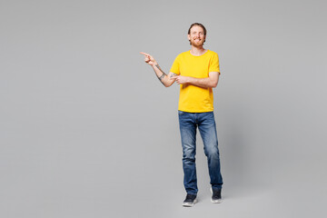 Wall Mural - Full body young man he wear yellow t-shirt casual clothes point index finger aside indicate on workspace area copy space mock up isolated on plain grey background studio portrait. Lifestyle concept.