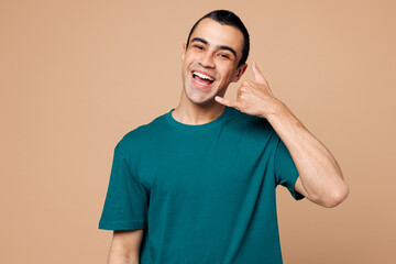 Young smiling happy middle eastern man wear blue t-shirt casual clothes doing phone gesture like says call me back isolated on plain pastel light beige background studio portrait. Lifestyle concept.