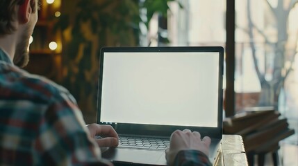 ver shoulder shot of a young man using computer laptop in front of an blank white computer screen in home