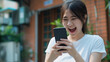 © tiagozr - Joyful Asian woman reacting to smartphone outdoors.