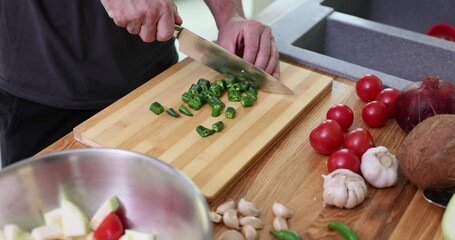 Wall Mural - Slicing chili peppers into thin rings on wooden board. Man prepares vegetable salad adding slight spice at home in kitchen slow motion