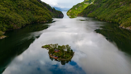 Wall Mural - A small island with two red houses is nestled in a calm fjord surrounded by verdant forested hills. Lovrafjorden, Norway