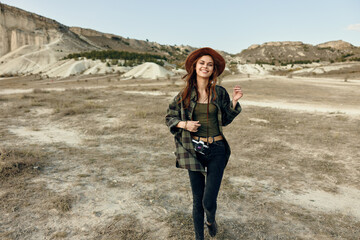 Wall Mural - Woman in plaid shirt and hat walking through desert landscape with mountains in background