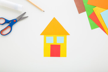 Wall Mural - House shape from colorful application paper, scissors, pencil and glue stick on light gray table background. Child making family home. Closeup. Top down view.