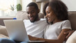 © Maksym - Husband and wife, a young African American couple, using a laptop and credit card for online shopping, sitting close on a comfortable sofa couch, enjoying their e-commerce experien