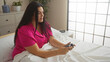 © Krakenimages.com - Woman playing video game while sitting on bed in modern bedroom, showcasing a young plus size female in comfortable pink pajamas indoors at home.