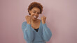 © Krakenimages.com - A cheerful african american woman in a blue sweater posing against a pink background with an affable smile.