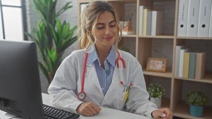 Sticker - A young blonde woman in a white coat with a stethoscope sits at a desk in a hospital room, representing healthcare professionalism.