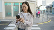 © Krakenimages.com - Chinese woman texting on smartphone while standing on a city street with pedestrians in the background