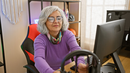 Sticker - A mature woman sits at a gaming setup in a well-lit room, enjoying video games with focus and joy.