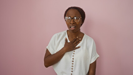 Canvas Print - Woman expressing surprised emotion with hand on chest, standing against isolated pink background, wearing glasses and white shirt