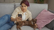© Krakenimages.com - A young beautiful caucasian woman relaxing with her dog on a couch at home while looking at her phone in the living room.