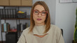 © Krakenimages.com - Attractive blonde woman with glasses in an office setting, sitting indoors, with shelves and files in the background, creating a professional and workspace atmosphere.