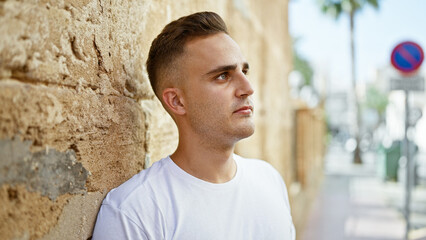 Poster - Handsome young man in casual attire leaning against an old city wall outdoors.