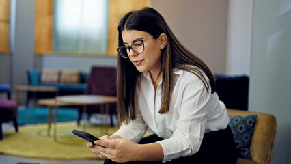 Poster - Young beautiful hispanic woman using smartphone sitting on a chair at the office