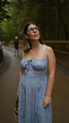 Wall Mural - Beautiful hispanic woman with glasses, smiling confidently as she stands amongst kyoto's lush bamboo forest, looking around, full of joy and amazement.