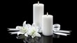 © lililia - Two white candles with flames are burning, set on a black surface with a white lily flower and a bow