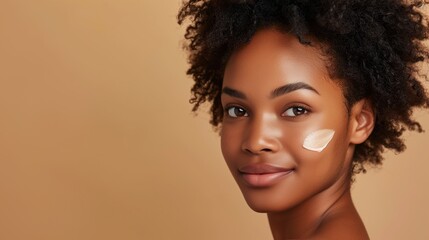 Wall Mural - Black woman with moisturizer on cheek, closeup studio portrait on beige background with copy space, female skincare concept