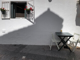 Window with flowers and table with wooden chairs on a street in Vejer de la Frontera, in the province of Cadiz, Andalusia, Spain.