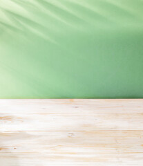 Wall Mural - Blurred shadow of  leaves on the light green wall and table top in the foreground. Summer concept.