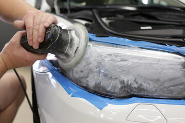 Cropped image of hands of male professional worker with orbital polisher in auto repair shop, polishing car headlight. Car wax polishing process. The process of polishing the headlights. 