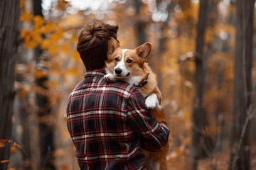 Man holding corgi in blurred autumn forest background. Friendship and pet love concept. Companion and friend. Man with his dog. Banner, poster