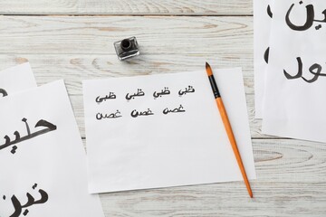 Wall Mural - Calligraphy. Papers with words Fig, Milk, Doctor in Arabian language, inkwell and brush on white wooden table, flat lay