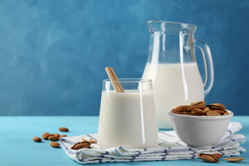 Sticker - Glass of almond milk, jug and almonds on light blue wooden table, space for text