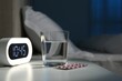 © New Africa - Insomnia treatment. Glass of water, pills and alarm clock on bedside table in bedroom at night