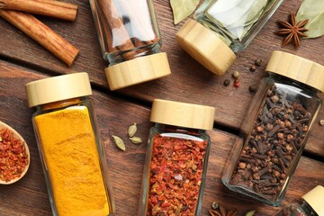 Wall Mural - Different spices in glass jars on wooden table, flat lay