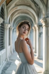 Young woman in light grey dress posing in an arched corridor. Elegance and architectural beauty concept