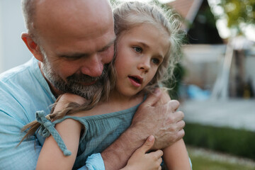 Wall Mural - Portrait of father embracing his beautiful daughter in the garden. Dad and daughter spending quality time together, bonding during summer evening.