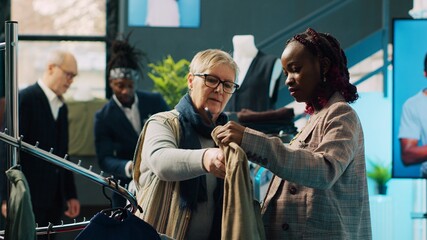 Sticker - African american retail clerk showing new fashion collection to senior client in department store at the mall. Pregnant assistant making color suggestions to regular customer, consumerism. Camera A.