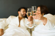 © AntonioDiaz - Joyful pair in bathrobes raising glasses of champagne during a romantic escape in a hotel suite