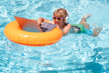 Wall Mural - Child swimming on an inflatable ring with a laptop water pool. Little freelancer using computer, remote working in swimming pool.